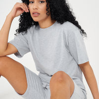 Woman in oversized grey cotton t-shirt and shorts, seated casual pose, displaying a modern fit.