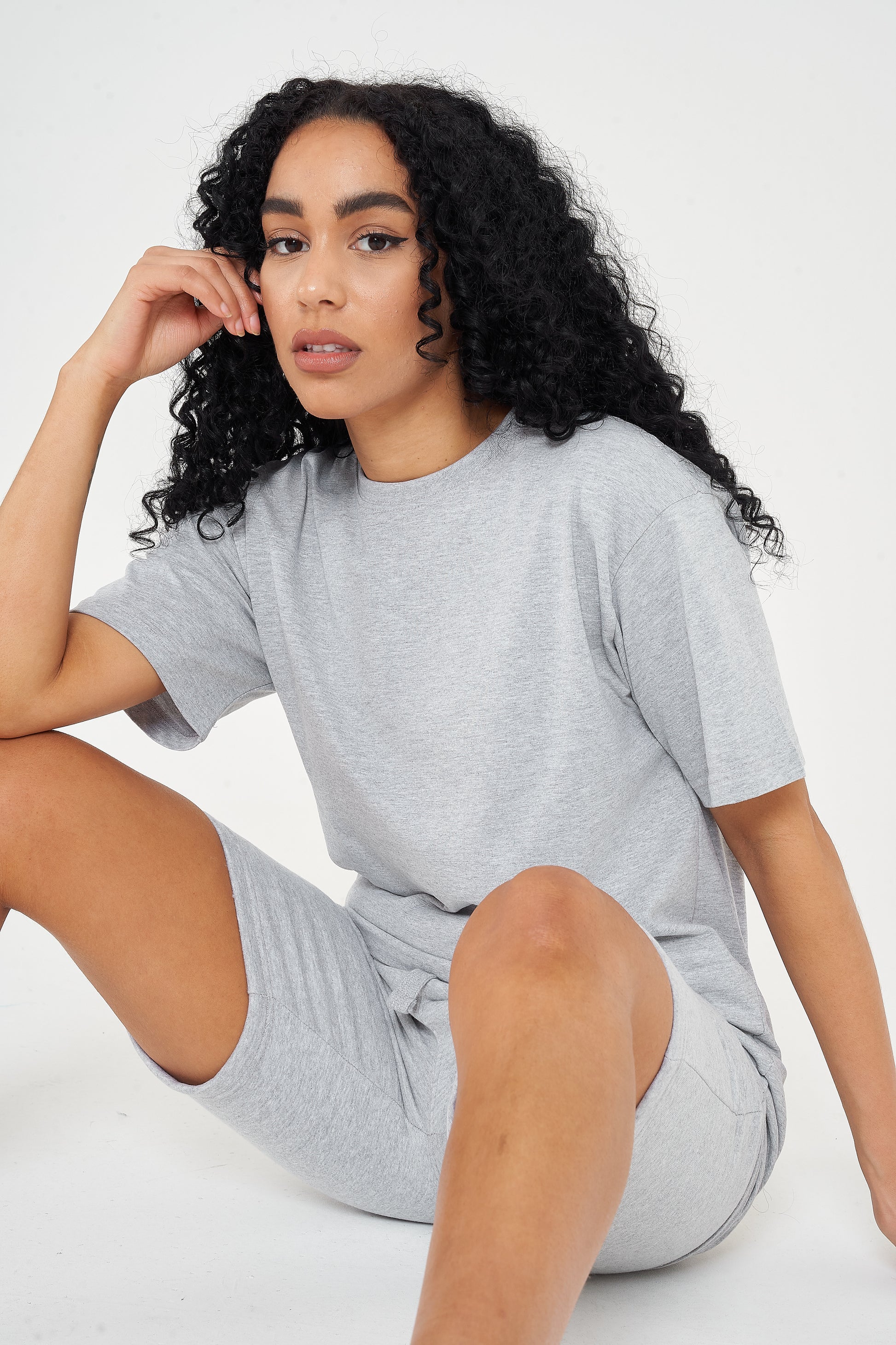 Woman in oversized grey cotton t-shirt and shorts, seated casual pose, displaying a modern fit.