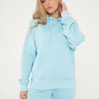 Woman modeling turquoise oversized hoodie in a sideways pose, showing roomy fit. 