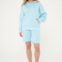 Woman wearing a turquoise oversized hoodie with matching shorts, standing front-facing. 