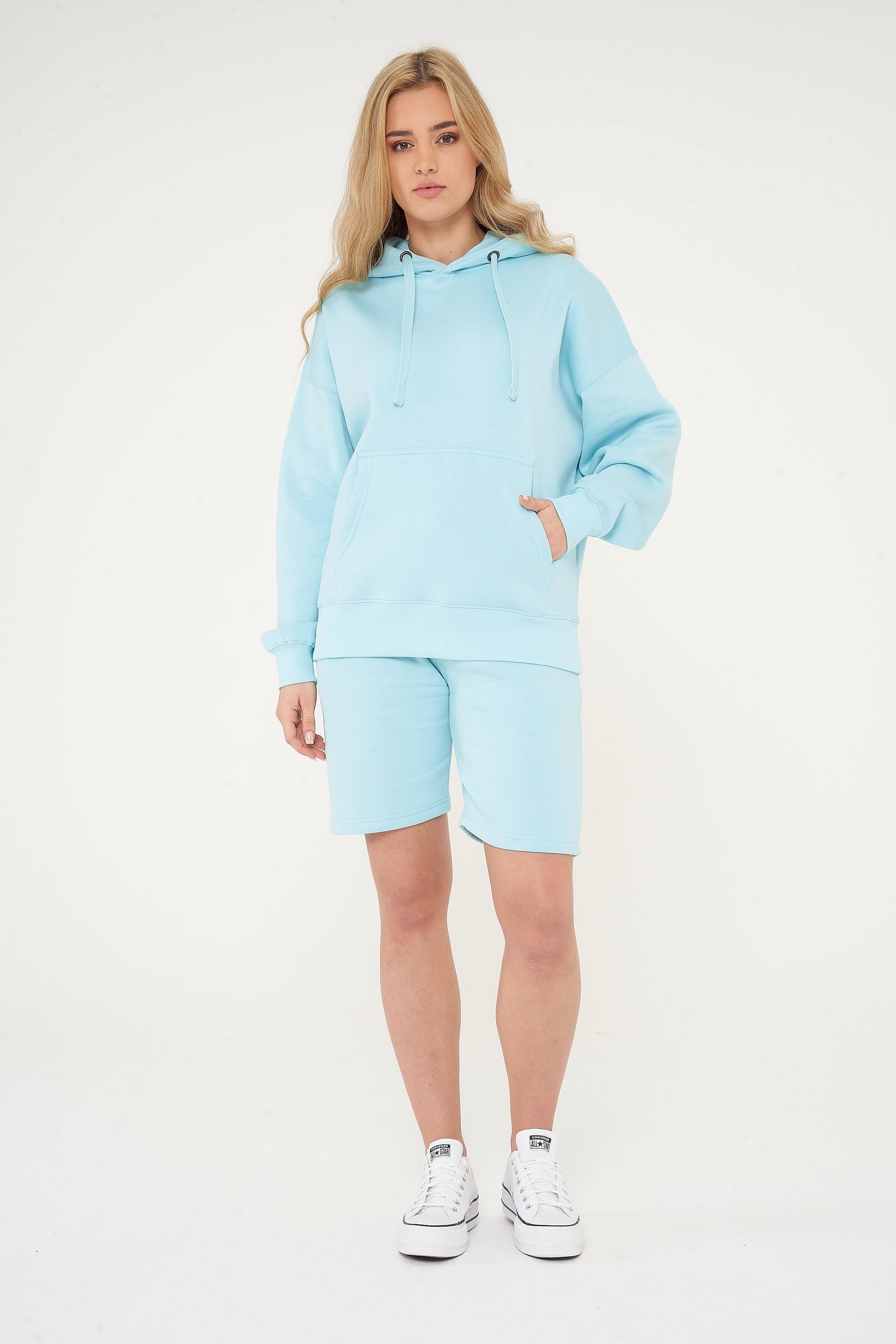 Woman wearing a turquoise oversized hoodie with matching shorts, standing front-facing. 