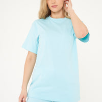 Woman in a turquoise oversized t-shirt with shorts, casual standing pose displaying color and silhouette.