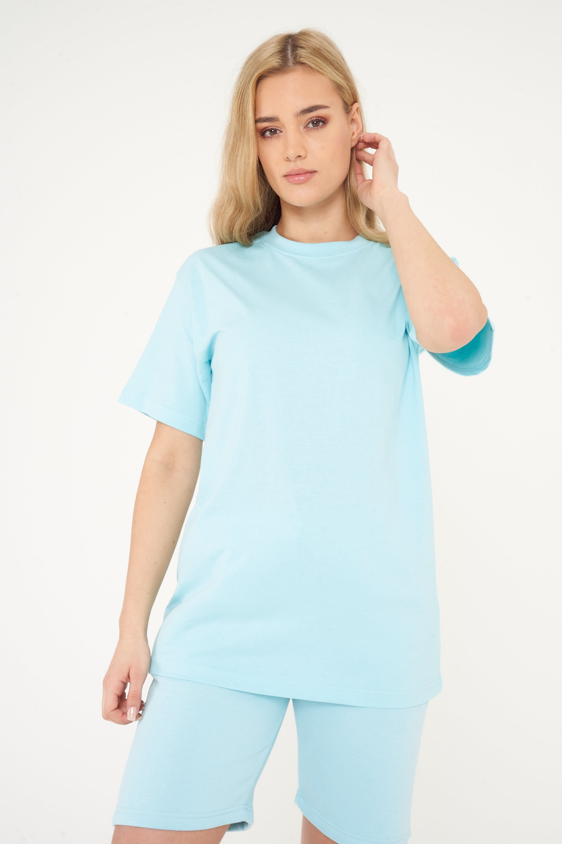 Woman in a turquoise oversized t-shirt with shorts, casual standing pose displaying color and silhouette.