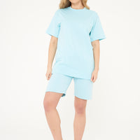 Woman wearing an oversized turquoise t-shirt and shorts, front-facing.