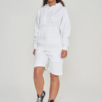 Woman wearing oversized white hoodie with casual shorts, standing front-facing. 