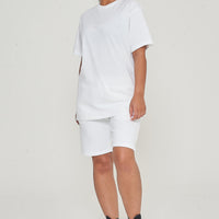 A Woman wearing an oversized white t-shirt with casual shorts, facing front. 