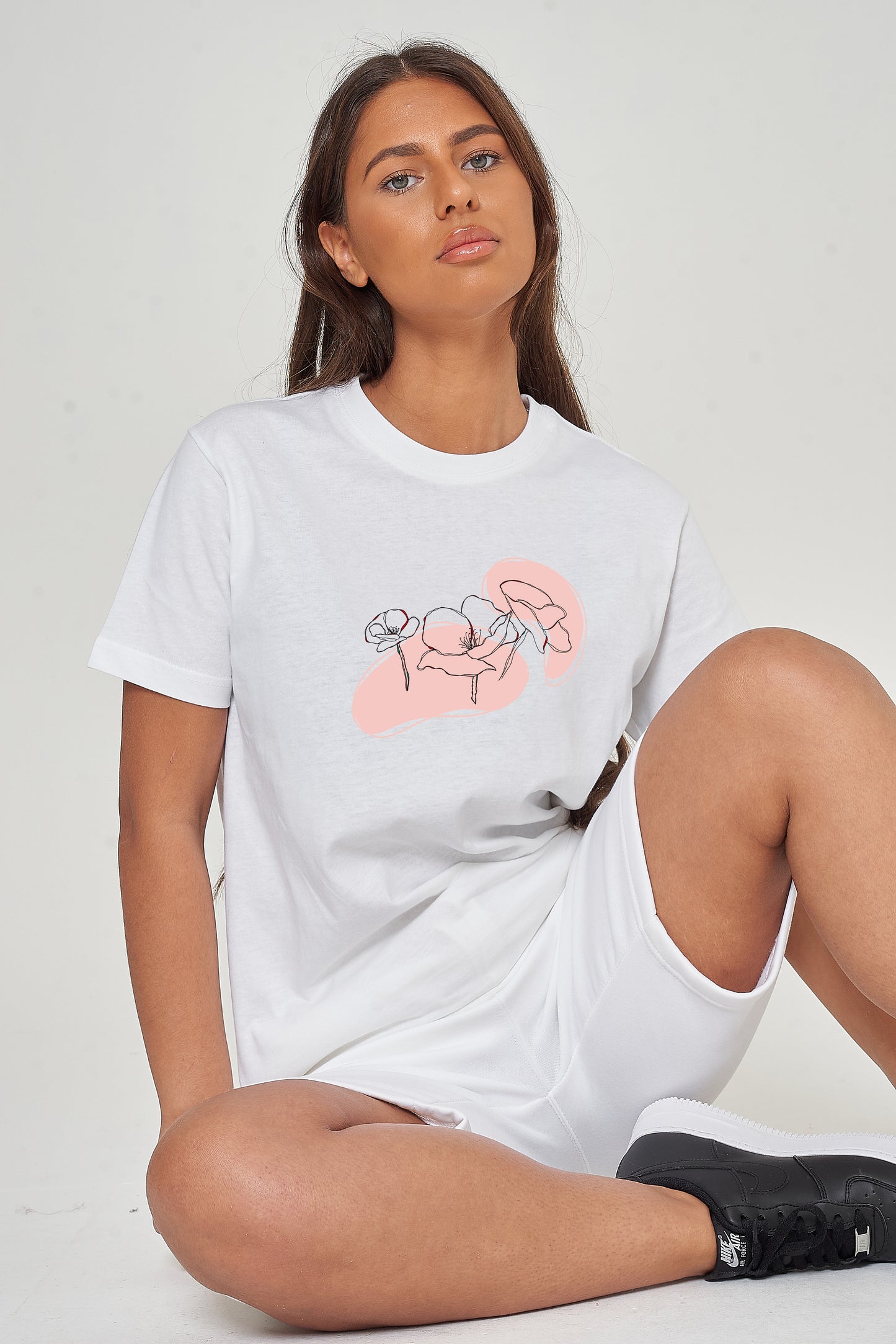 Woman wearing the white Pink Flower Paint Art T-Shirt styled with casual bottoms, highlighting the delicate front floral print and comfortable oversized fit.