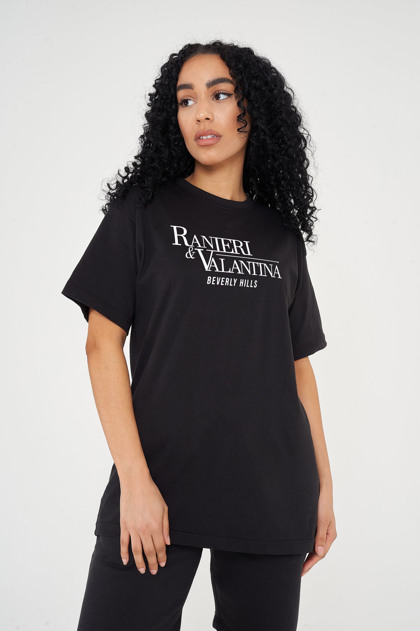 Woman wearing black oversized Signature Beverly Hills T-shirt, styled with casual shorts, showing front logo print.