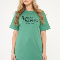 Woman wearing green oversized Signature Beverly Hills T-shirt, styled with casual shorts, showing front logo print.