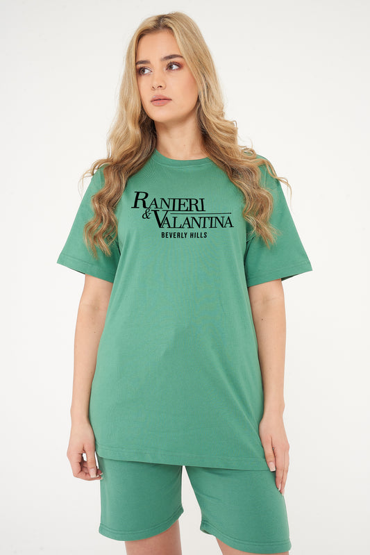 Woman wearing green oversized Signature Beverly Hills T-shirt, styled with casual shorts, showing front logo print.