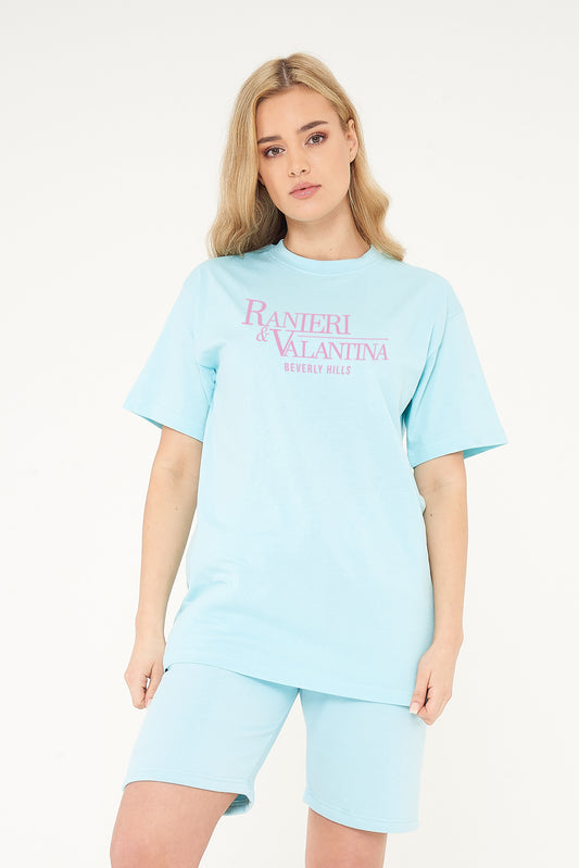 Woman wearing turquoise oversized Signature Beverly Hills T-shirt and shorts, highlighting front logo print.