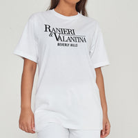 A Woman wearing a white oversized Signature Beverly Hills T-shirt and shorts, showcasing the front logo and casual styling.