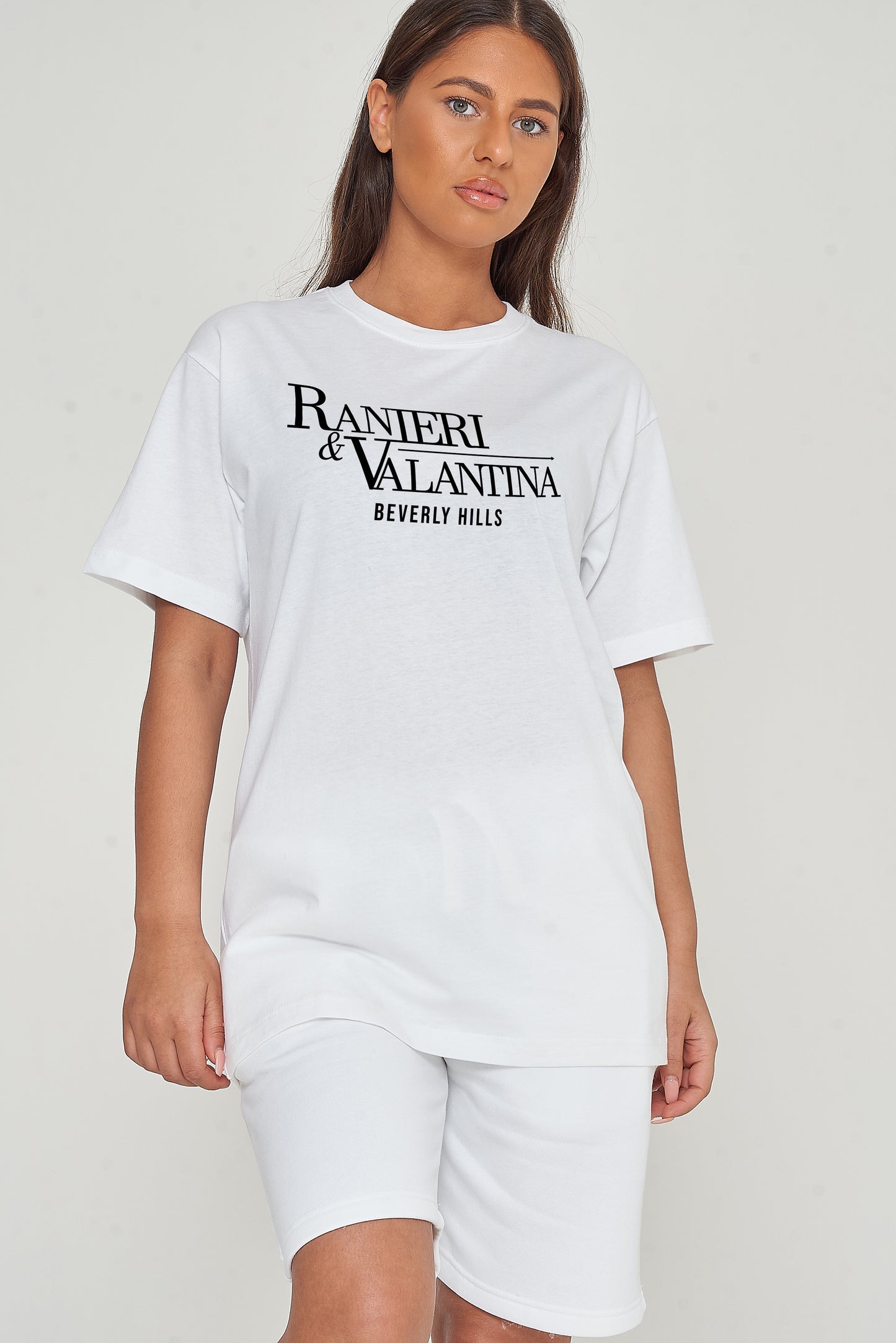 A Woman wearing a white oversized Signature Beverly Hills T-shirt and shorts, showcasing the front logo and casual styling.