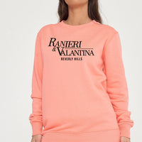 Woman wearing coral Signature Beverly Hills sweatshirt, styled with matching shorts, highlighting city-inspired casual style.