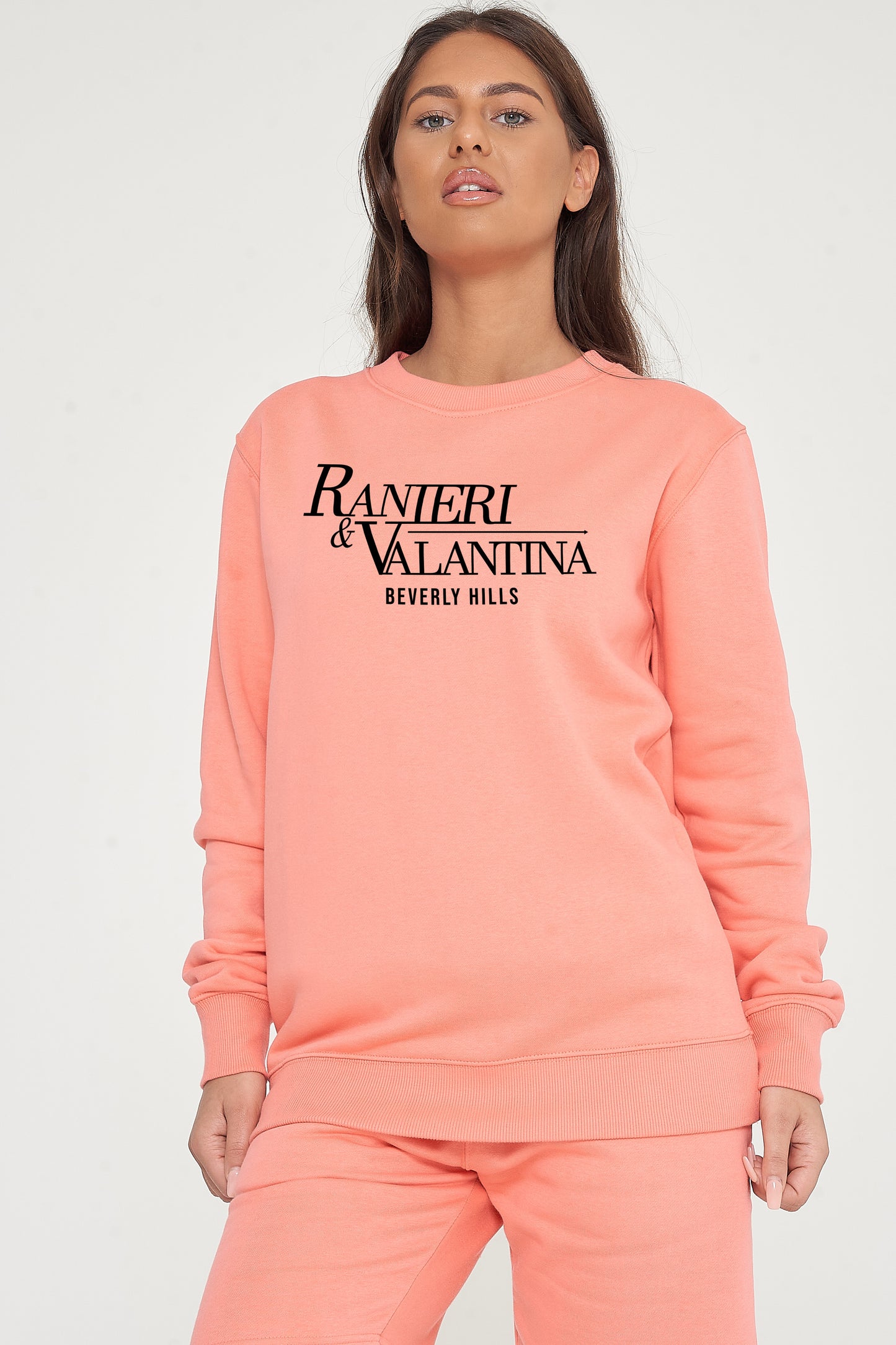 Woman wearing coral Signature Beverly Hills sweatshirt, styled with matching shorts, highlighting city-inspired casual style.