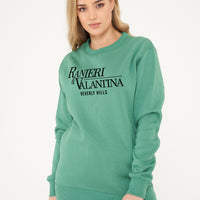 Woman wearing green Signature Beverly Hills sweatshirt, styled with casual leggings.
