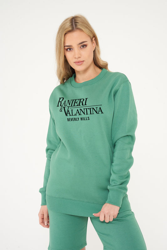 Woman wearing green Signature Beverly Hills sweatshirt, styled with casual leggings.