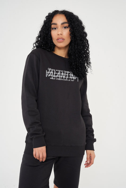 Woman wearing the black Strong Woman Sweatshirt styled with casual bottoms, highlighting the empowering front print and comfortable fit.