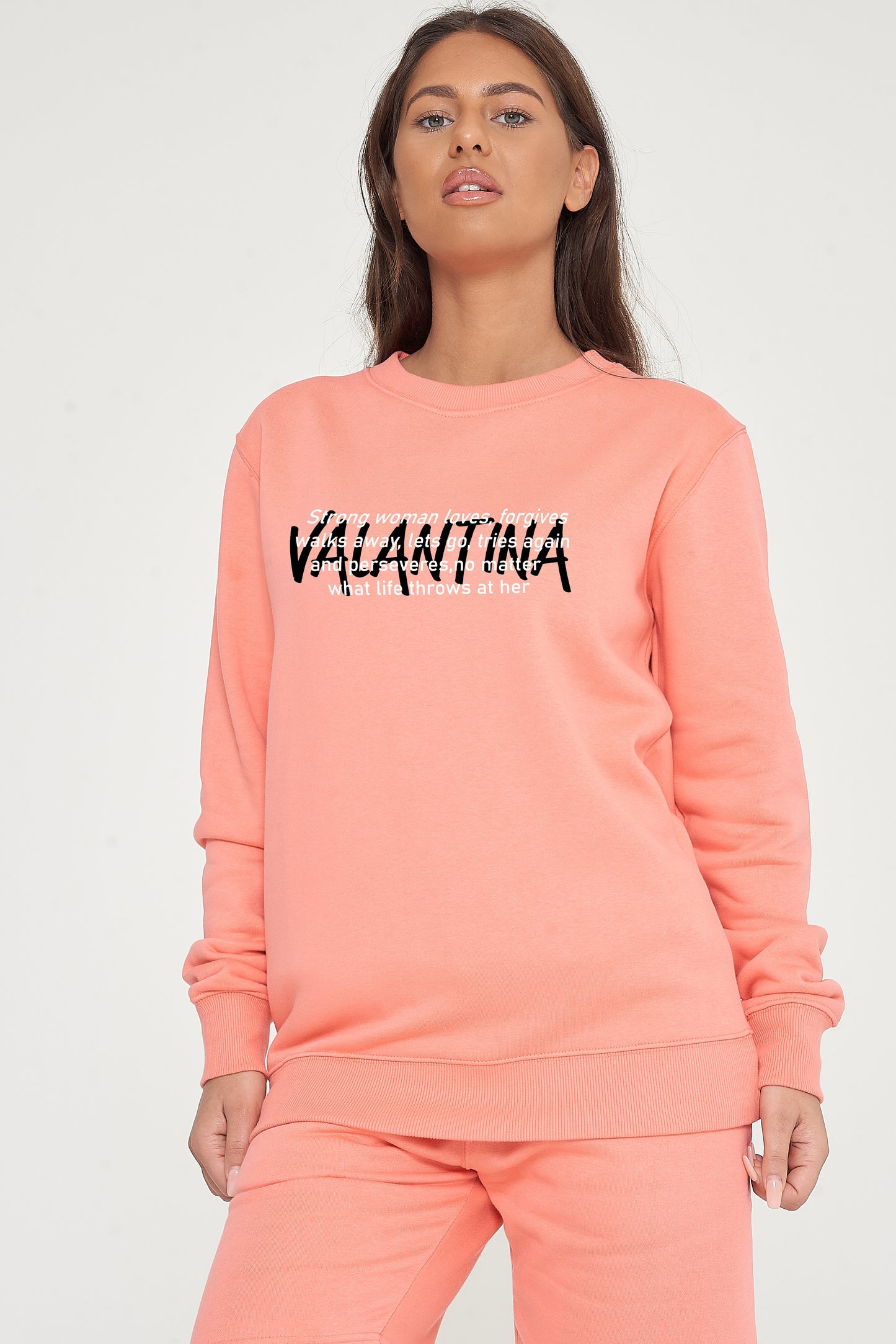 Woman wearing the coral Strong Woman Sweatshirt styled with casual bottoms, showcasing the empowering front graphic and comfortable fit.