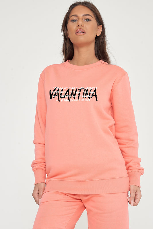 Woman wearing the coral Strong Woman Sweatshirt styled with casual bottoms, showcasing the empowering front graphic and comfortable fit.