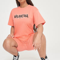 Woman wearing the coral Strong Women T-Shirt styled with casual bottoms, highlighting the empowering front text and comfortable silhouette.