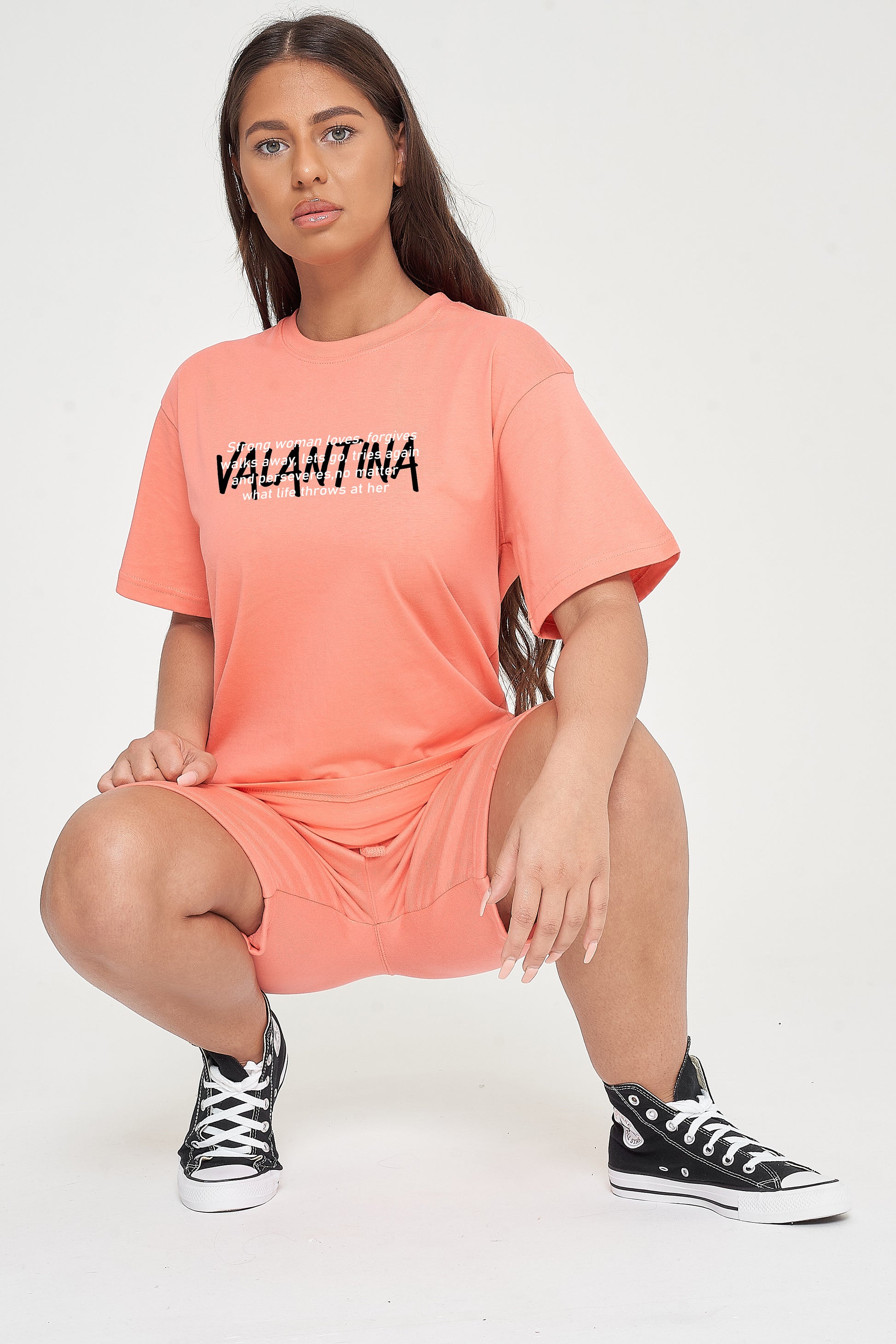Woman wearing the coral Strong Women T-Shirt styled with casual bottoms, highlighting the empowering front text and comfortable silhouette.