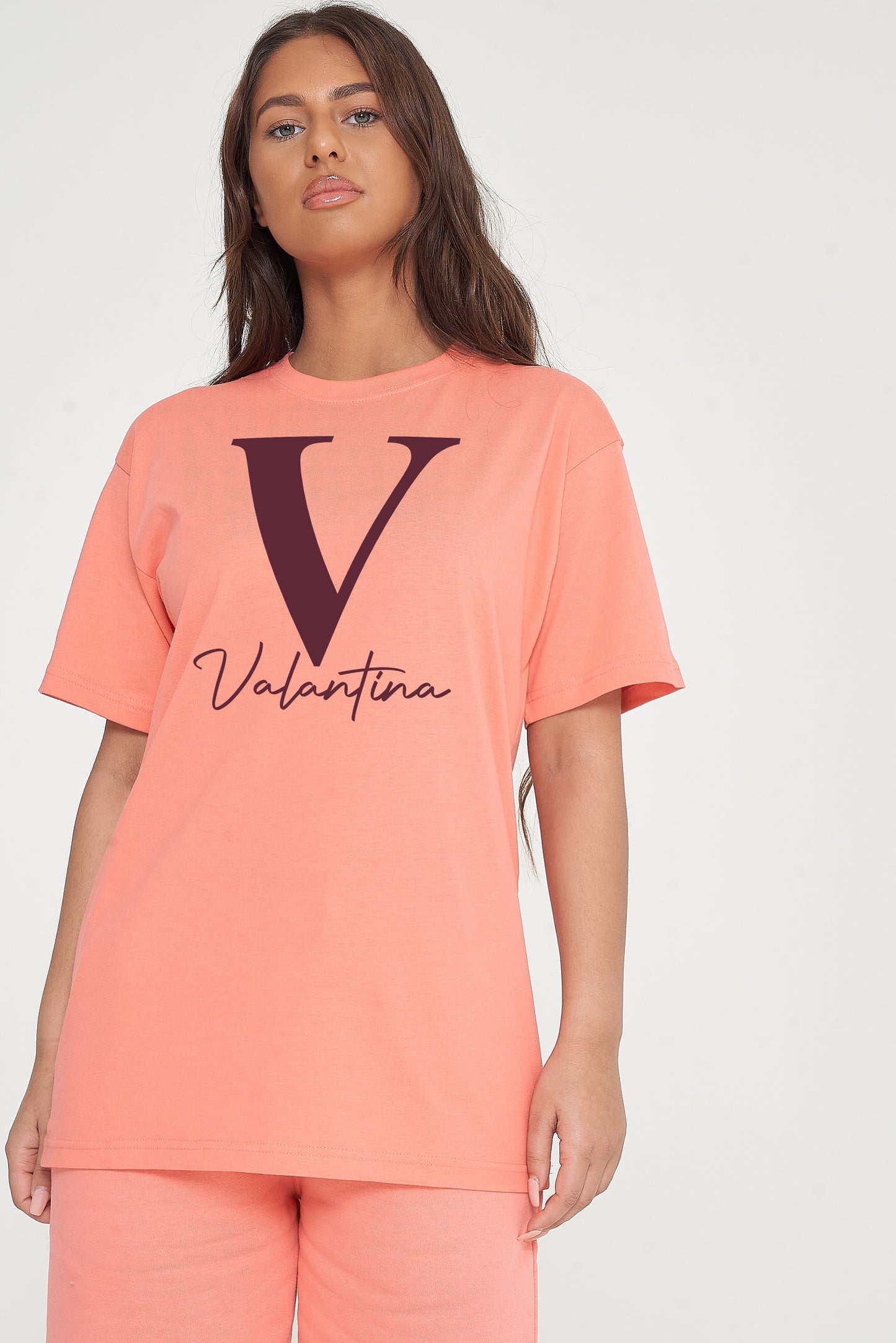 Woman wearing coral Valantina Signature Graphic T-Shirt styled with casual bottoms, highlighting the front signature print and comfortable silhouette.
