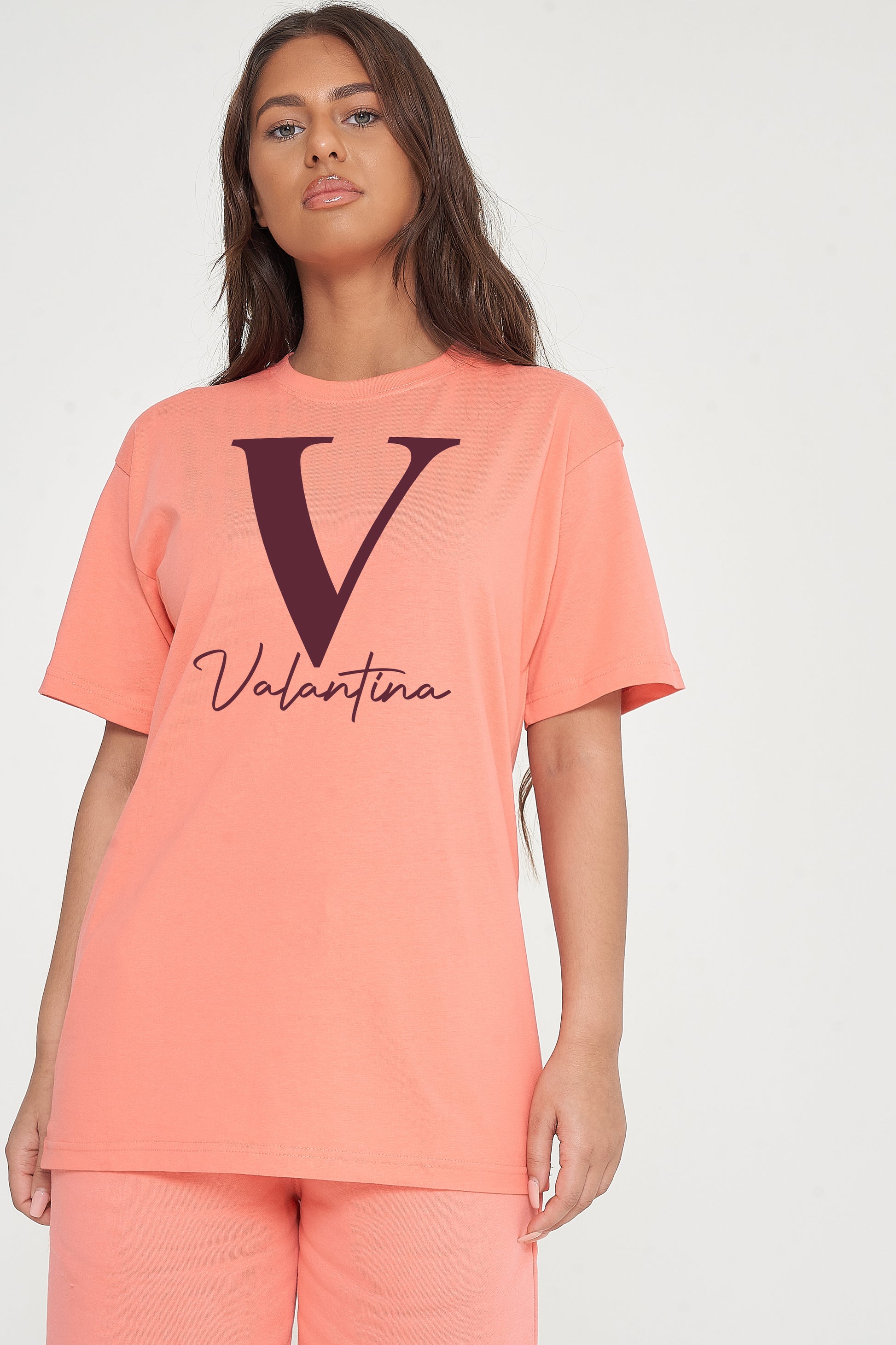 Woman wearing coral Valantina Signature Graphic T-Shirt styled with casual bottoms, highlighting the front signature print and comfortable silhouette.