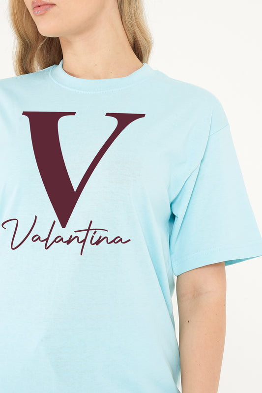Woman wearing the turquoise Valantina Signature Graphic T-Shirt styled with casual bottoms, highlighting the front signature print and comfortable oversized silhouette.