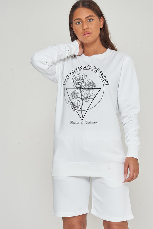Female model wearing white Wild Roses sweatshirt styled with shorts, standing against a plain background.