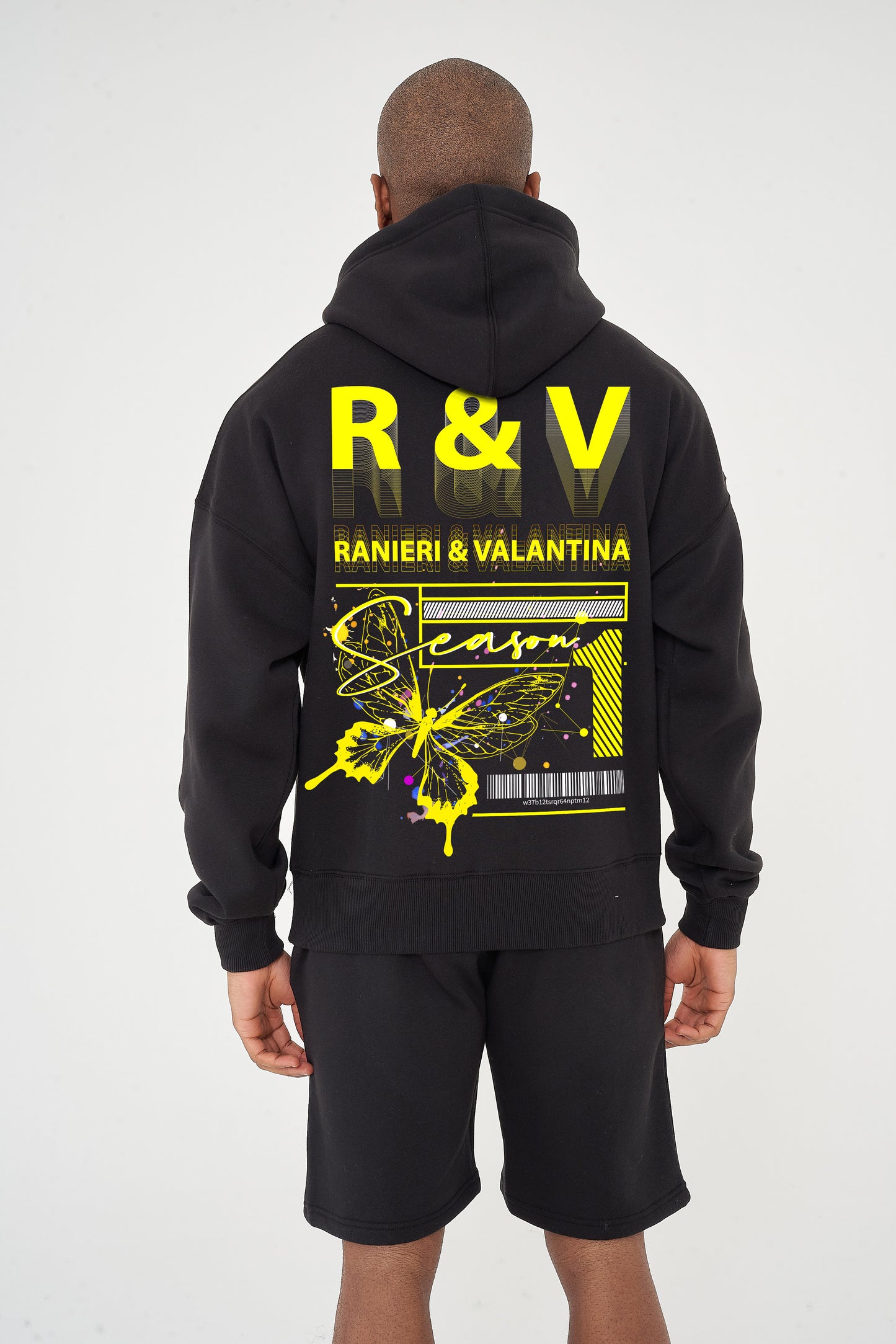 Rear view of male model wearing black oversized hoodie with striking yellow butterfly graphic and R&V print – oversized fit.